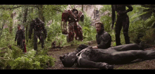 a man in a black suit is laying on the ground surrounded by a group of people