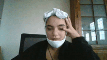 a woman wearing a mask and a white headband holds her hand to her forehead