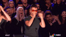 a man wearing red sunglasses is dancing in front of a crowd with nbc written on the bottom right