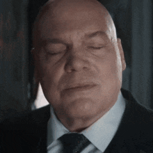 a bald man wearing a suit and tie with his eyes closed