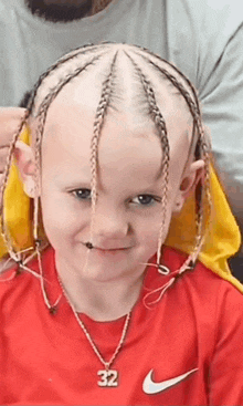 a little boy with braids on his head is wearing a red nike shirt and a necklace with the number 32 on it .