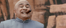 a bald man is smoking a cigar in front of a wall