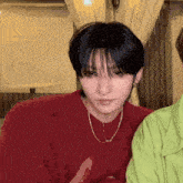 a young man wearing a red sweater and a necklace looks at the camera