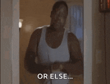 a man in a white tank top is standing in a doorway and talking to someone .