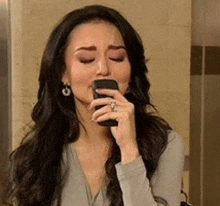 a woman with long hair is holding a cell phone in her mouth .