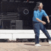 a man in a blue shirt is dancing on a stage in front of an american flag
