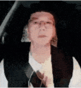 a man wearing glasses and a hat is sitting in the driver 's seat of a car and looking at the camera .