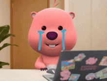 a pink teddy bear is crying in front of a laptop computer .