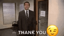 a man in a suit and tie is standing in front of a door with a thank you emoji .