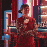 a woman with glasses is standing in a bar with her arms crossed .