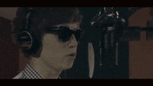 a man wearing headphones and sunglasses sings into a microphone