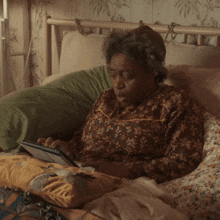 an elderly woman laying on a bed using a tablet