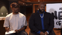 two men are sitting in front of a sign that says " ae "