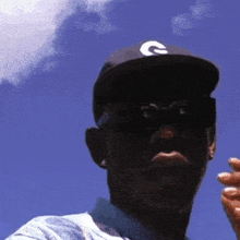a man wearing a baseball cap and sunglasses is looking at the camera .