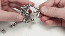 a person is playing with a metal puzzle with balls on the table