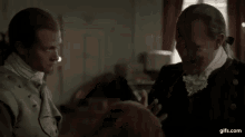 two men in historical costumes are sitting next to each other in a room and talking .