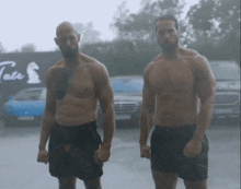 two shirtless men are standing in the rain in front of a tate sign