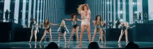 a group of women are dancing on a stage while a woman sings