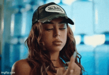 a woman wearing a von dutch hat is smoking a cigarette and making a funny face .