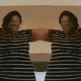 two people wearing striped shirts are shaking hands in front of a mirror .