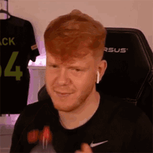 a man with red hair and a beard is sitting in a chair wearing headphones and a black shirt .
