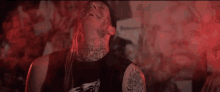 a man with long hair and a tattoo on his neck is standing in front of a wall .