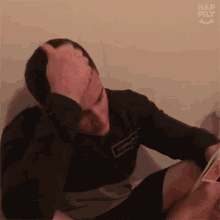 a man is sitting on the floor holding his head while looking at a cell phone .
