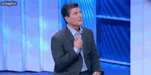 a man in a suit and tie is sitting in front of a blue curtain .