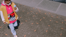 a man in a pink hoodie and a yellow jacket is walking on a brick sidewalk