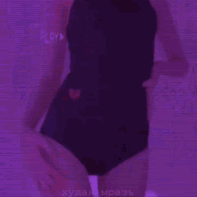 a woman is standing in a room with a purple background . she is wearing black shorts and a white bra .