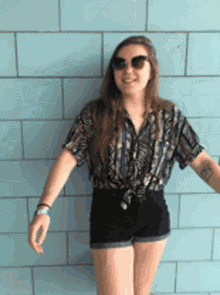a woman wearing shorts and sunglasses is standing in front of a blue wall
