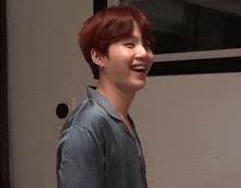 a young man with red hair is wearing a blue shirt and smiling while standing in a room .