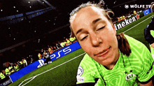 a woman in a green shirt is on a soccer field with a heineken sign behind her