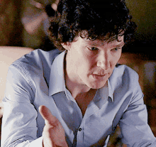 a man with curly hair is wearing a light blue shirt and giving a thumbs up