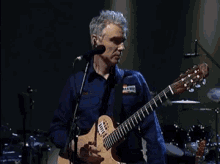 a man in a blue shirt is playing a guitar and singing into a microphone .