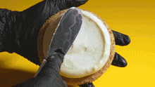 a person wearing black gloves is spreading a white frosting on a cookie