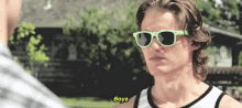 a man wearing green sunglasses and a white tank top is talking to a man .