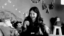 a black and white photo of a girl sitting on a bed surrounded by stuffed animals .