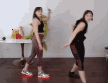 two women are dancing in front of a table with a stuffed animal on it