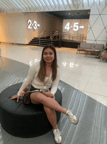 a woman sits on a black ottoman in front of a sign that says 2-3 4-5