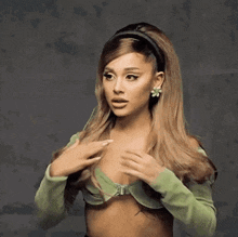 ariana grande is wearing a green off the shoulder top and earrings .