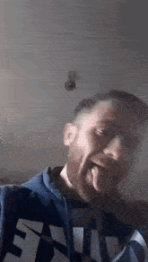 a man with a beard is sticking his tongue out and wearing a blue hoodie .