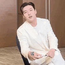 a man in a white suit is sitting in a chair holding a pen and making a funny face .