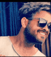 a man with a beard wearing sunglasses is smiling and looking at the camera .