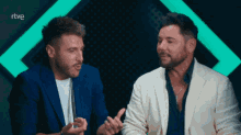 two men are sitting next to each other in front of a green light and the word rtve is on the bottom right