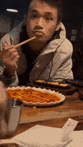 a man sitting at a table with a plate of food and chopsticks in his hand