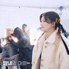 a woman in a white fur coat stands in front of a group of people with korean writing on the bottom