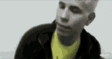 a man wearing a yellow shirt and a black jacket is looking at the camera .