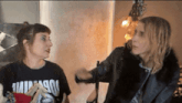 a woman wearing a shirt that says ' nirvana ' on it talks to another woman
