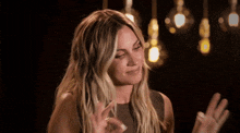 a woman is making a funny face with her hands outstretched in front of a bunch of lights hanging from the ceiling .